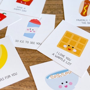 May include: A set of ten greeting cards with cute food illustrations and puns. The cards are white with black text and feature a banana, a waffle, a hot dog, a slushie, a bowl of cereal, and a red pepper.