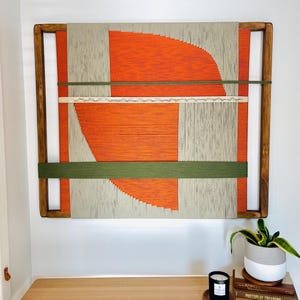 a wooden table with a plant and a candle on it, set against a white wall with a large abstract painting hanging above.