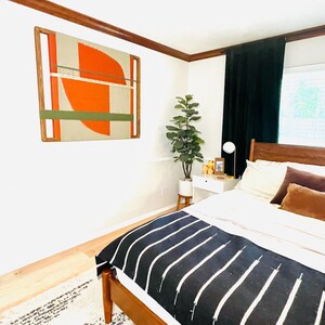 a modern bedroom with a large bed, a wooden headboard, and a colorful abstract painting on the wall. The room has a minimalist and stylish design, with a wooden floor and a large window providing natural light.