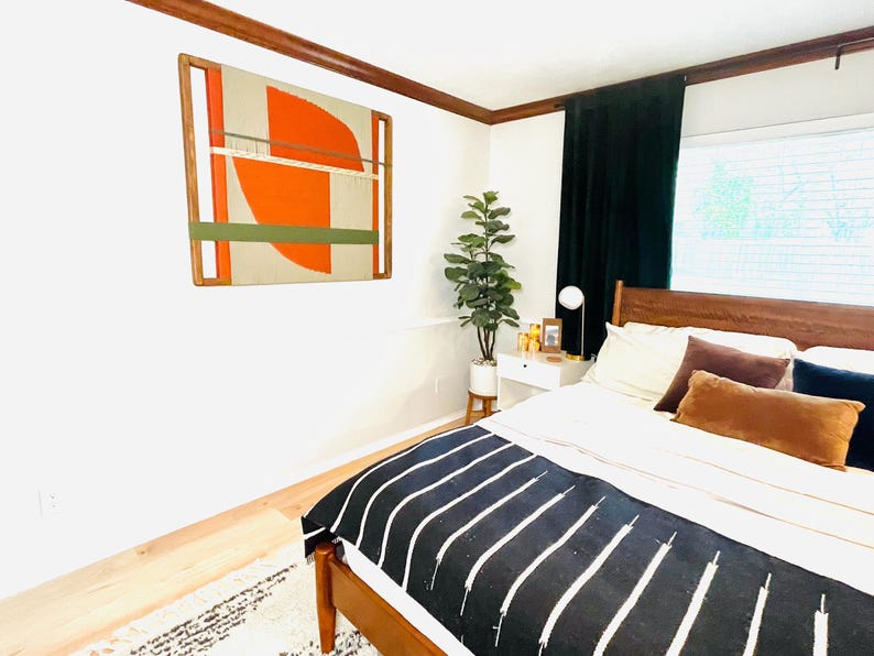 a modern bedroom with a large bed, a wooden headboard, and a colorful abstract painting on the wall. The room has a minimalist and stylish design, with a wooden floor and a large window providing natural light.