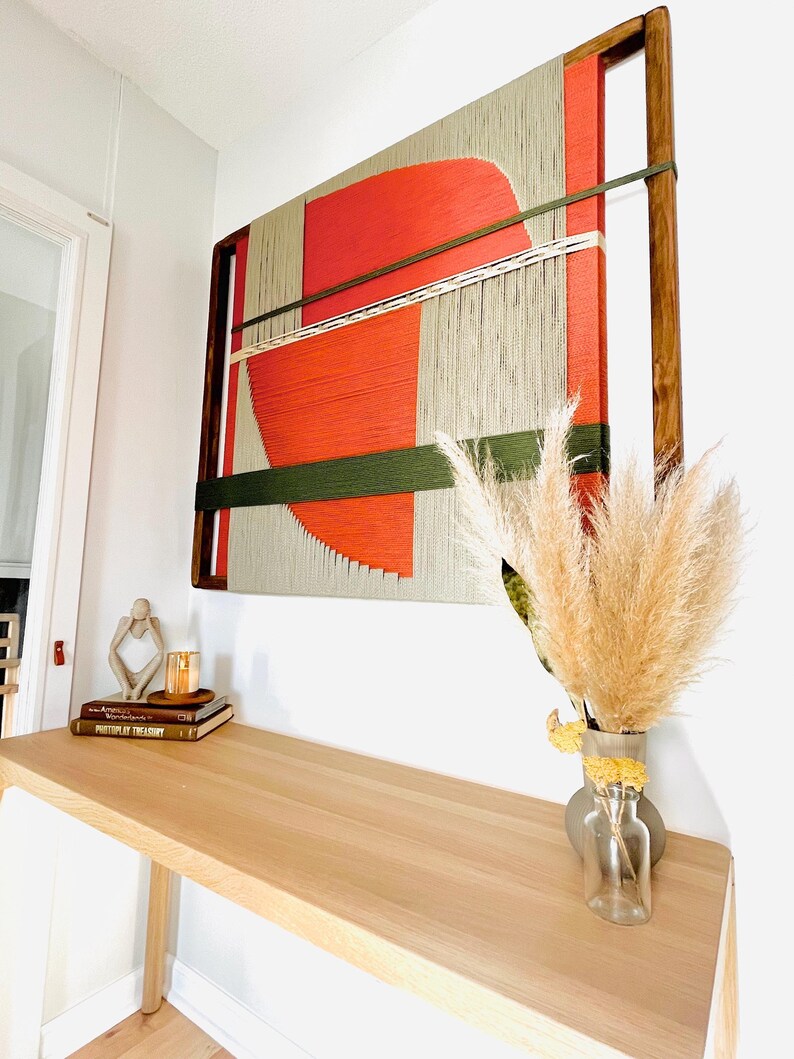 a wooden desk with a vase of dried flowers, a stack of books, and a large abstract painting hanging on the wall above the desk.