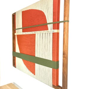 a wooden frame with a vibrant abstract artwork hanging on the wall. The artwork consists of a large red shape and a white and green striped pattern, creating a striking contrast. The wooden frame adds a rustic touch to the overall composition.