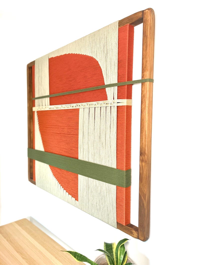 a wooden frame with a vibrant abstract artwork hanging on the wall. The artwork consists of a large red shape and a white and green striped pattern, creating a striking contrast. The wooden frame adds a rustic touch to the overall composition.