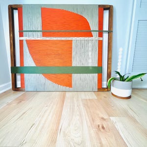 a wooden frame with a vibrant abstract painting on it, placed on a wooden floor next to a potted plant.