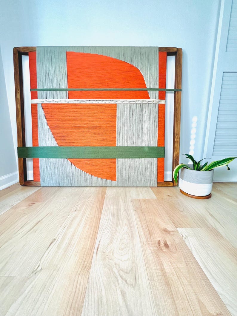 a wooden frame with a vibrant abstract painting on it, placed on a wooden floor next to a potted plant.