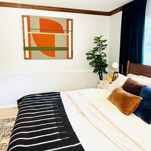 a well-decorated bedroom with a large bed, a colorful abstract painting on the wall, and a potted plant on a side table.