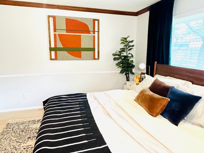a well-decorated bedroom with a large bed, a colorful abstract painting on the wall, and a potted plant on a side table.