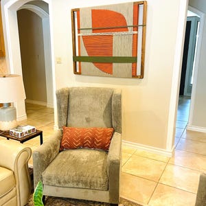 a cozy living room with a beige armchair, a wooden coffee table, and a large abstract painting on the wall.
