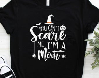 Può includere: Maglietta nera con un design grafico bianco di un cappello da strega, una zucca e il testo "You Can't Scare Me I'm A Mom".