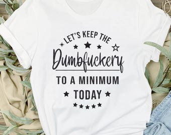 May include: White t-shirt with black text that reads "* LET'S KEEP THE Dumbfuckery TO A MINIMUM TODAY *" with stars around the text.