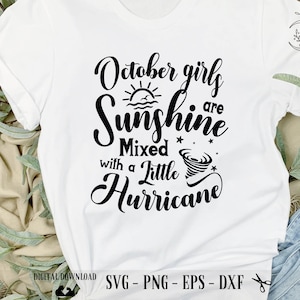 May include: White t-shirt with black text that reads "October girls are sunshine mixed with a little hurricane". The text includes a sun, a wave, and a tornado graphic.