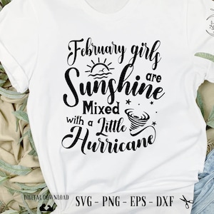 Könnte beinhalten: Weißes T-Shirt mit schwarzem Text, der "February girls are sunshine mixed with a little hurricane" lautet. Der Text ist in einer kursiven Schriftart und enthält ein Sonnen- und ein Tornado-Motiv.