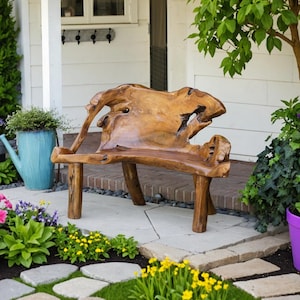 May include: A handcrafted wooden bench with a unique, organic design. The bench is made of light brown wood and features a natural, textured surface. It has a curved back and sturdy legs. The bench is placed on a stone patio, surrounded by colorful flowers and greenery.