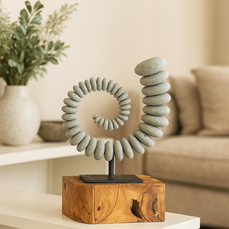 May include: A decorative sculpture featuring a spiral design made of gray stones. The stones are stacked on a black metal stand, which is mounted on a wooden block. The sculpture is a unique home decor item.
