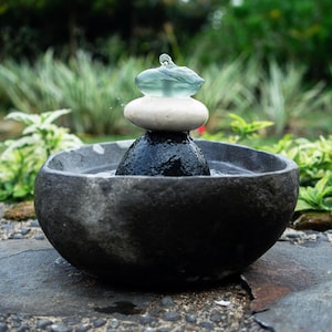 Handcrafted Zen Balance Cairns Fountain with a carved natural river stone base, stacked cairn of river stone, white jasper, and recycled aqua glass top. Creates soothing water flow and relaxing sound, ideal for meditation, relaxation, or mindful home décor. Includes 6 ft cord low-voltage pump with adjustable flow. Perfect for indoor use or covered patios, adding a calming focal point to gardens, desks, or living spaces. Unique, nature-inspired gift for spa lovers and meditation spaces.