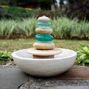 Hand-carved white marble fountain with luminous natural stone base and stacked cairns made from polished jasper and translucent recycled blue glass. Water flows gently over each tier, creating a soothing rippling sound and serene visual effect. A heavy, durable tabletop fountain perfect for meditation, yoga spaces, spa-inspired décor, or as a calming centerpiece for living rooms, covered patios, or garden nooks. Unique handmade design with clean cord-free look.