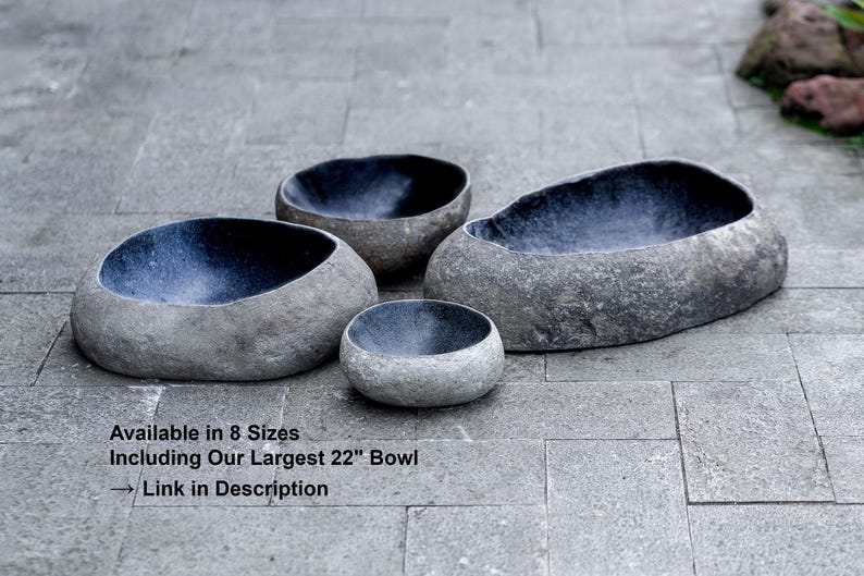 Multiple river stone bird bath bowls displayed together outdoors, showing a full range of sizes from small to extra-large. Each bowl features a hand-carved natural stone exterior with a smooth, dark polished interior. The group photo highlights variations in shape, thickness, and color across the collection. Perfect for showcasing all available sizes and the organic, heavy, durable nature of genuine river stone garden bowls.