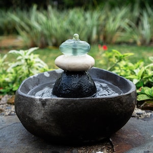 Handcrafted Zen Balance Cairns Fountain with a carved natural river stone base, stacked cairn of river stone, white jasper, and recycled aqua glass top. Creates soothing water flow and relaxing sound, ideal for meditation, relaxation, or mindful home décor. Includes 6 ft cord low-voltage pump with adjustable flow. Perfect for indoor use or covered patios, adding a calming focal point to gardens, desks, or living spaces. Unique, nature-inspired gift for spa lovers and meditation spaces.