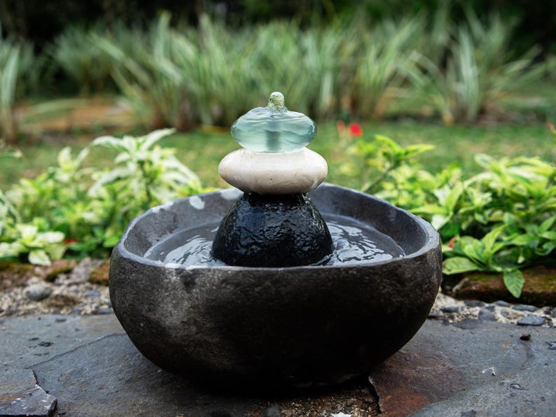 Handcrafted Zen Balance Cairns Fountain with a carved natural river stone base, stacked cairn of river stone, white jasper, and recycled aqua glass top. Creates soothing water flow and relaxing sound, ideal for meditation, relaxation, or mindful home décor. Includes 6 ft cord low-voltage pump with adjustable flow. Perfect for indoor use or covered patios, adding a calming focal point to gardens, desks, or living spaces. Unique, nature-inspired gift for spa lovers and meditation spaces.