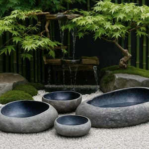 May include: A serene outdoor scene features four gray stone bowls of varying sizes, with dark blue interiors, arranged on a bed of white pebbles. A small waterfall flows from a wooden structure, and a bonsai tree and green bamboo complete the zen garden.