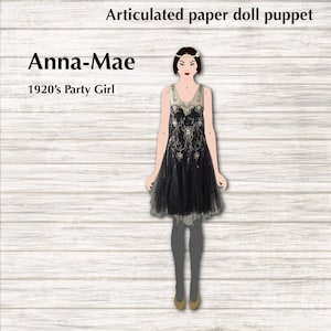 Könnte beinhalten: Gelenkige Papierpuppe einer Frau in einem schwarzen Flapper-Kleid mit goldenen Verzierungen. Die Puppe heißt Anna-Mae und ist als „Party Girl der 1920er Jahre“ gekennzeichnet.