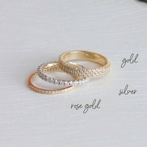 May include: Three eternity bands with a row of small clear stones. The bands are in rose gold, silver, and gold.