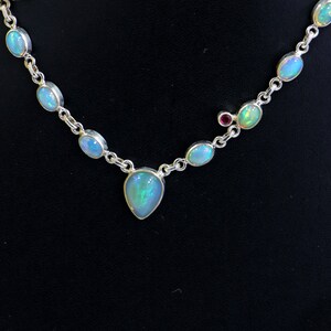 May include: A silver necklace with a teardrop-shaped opal pendant and smaller opal stones along the chain. A small red stone is also visible on the chain.