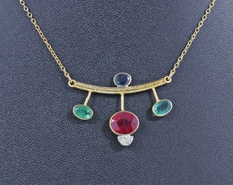 May include: A gold necklace with a curved bar and five dangling gemstones. The gemstones are red, green, and blue.