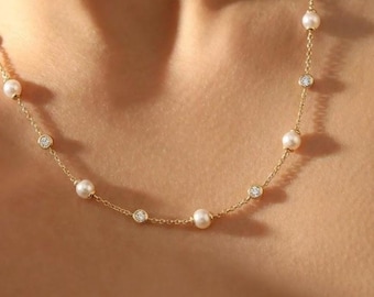 May include: A delicate gold chain necklace featuring a series of evenly spaced white pearls and small, round, clear, faceted stones set in gold bezels, creating a repeating pattern along the length of the fine metal link chain.