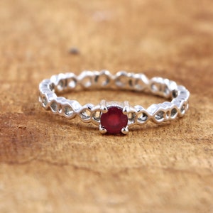 Könnte beinhalten: Ein silberner Ring mit einem filigranen, durchbrochenen Design und einem einzigen, runden, roten Rubin-Edelstein in der Mitte.