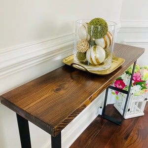 May include: A dark brown wooden console table with black metal legs. The table has a decorative tray with a glass vase filled with green and white decorative balls.