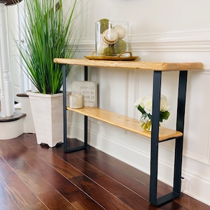 May include: A wooden console table with a black metal frame. The table has a single shelf and is decorated with a glass vase filled with green and white decorative balls and a sign that reads "grow old along with me the best is to be..."