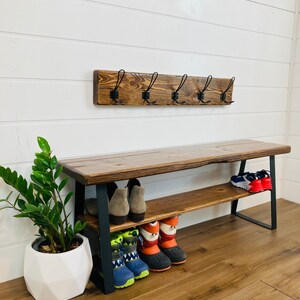 May include: A wooden bench with a metal frame and a shelf for storing shoes. The bench has a rustic brown finish and the metal frame is black. There are several pairs of shoes on the shelf, including boots, sneakers, and sandals.