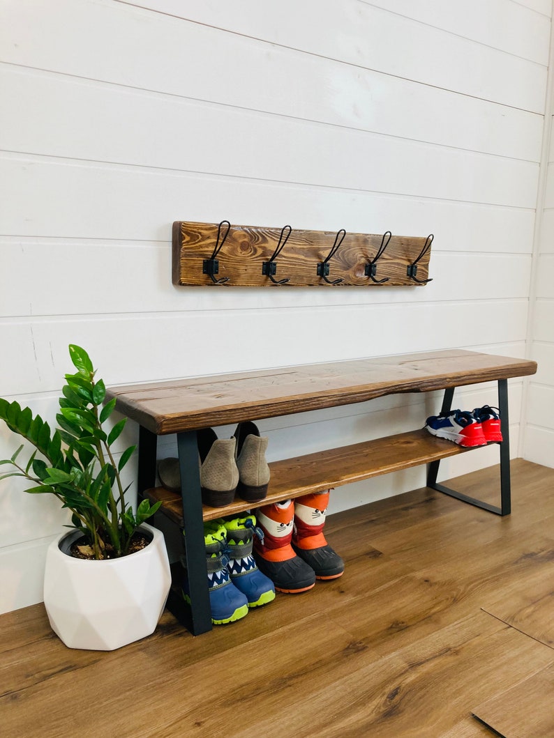 May include: A wooden bench with a metal frame and a shelf for storing shoes. The bench has a rustic brown finish and the metal frame is black. There are several pairs of shoes on the shelf, including boots, sneakers, and sandals.