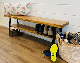 May include: A wooden bench with a shelf underneath. The bench has a dark brown stain and black metal legs. There are shoes on the shelf and a basket of shoes on the floor.
