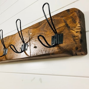 May include: A rustic wooden coat rack with four black metal hooks. The wood has a dark brown stain and a natural, reclaimed look.
