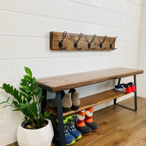 May include: A wooden bench with a metal frame and two shelves for storing shoes. The bench has a rustic brown finish and the metal frame is black. There are hooks on the wall above the bench.