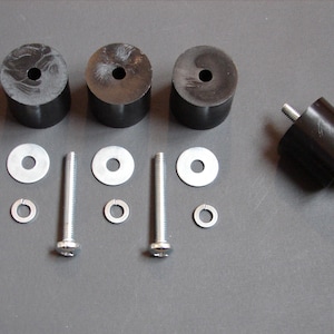 May include: Four black rubber feet with a hole in the center, three silver screws with washers, and one silver screw with a washer and a nut.