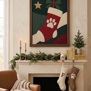 May include: A framed wall art piece featuring a red Christmas stocking with a white paw print, a green bow, and a gold star against a dark green background. Below, two knit stockings hang from a mantel, one cream with a red letter F and one brown with a white paw print.