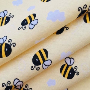 May include: Yellow fabric with a repeating pattern of cartoon bumblebees. The fabric has the text "Bumblebee Breeze" printed on it.