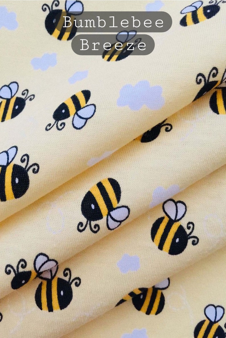 May include: Yellow fabric with a repeating pattern of cartoon bumblebees. The fabric has the text "Bumblebee Breeze" printed on it.