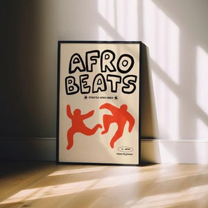 May include: A framed poster with the words "AFRO BEATS" in large, black, bubble letters. Below the text are two orange figures in motion. The poster is leaning against a white wall, with sunlight streaming across the wooden floor.
