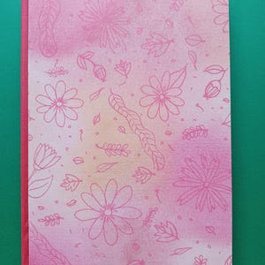 Può includere: Un quaderno di acquerello rosa e giallo con un design floreale. Il quaderno ha una rilegatura rossa e un segnalibro a nastro rosso.