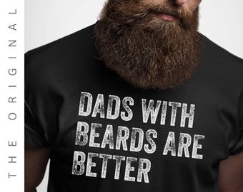 Puede incluir: Camiseta negra con la frase "DADS WITH BEARDS ARE BETTER" en letras blancas desgastadas. La imagen muestra un primer plano de la camiseta, con la barba y gafas de sol de un hombre visibles. Las palabras "THE ORIGINAL" están impresas verticalmente a la izquierda.