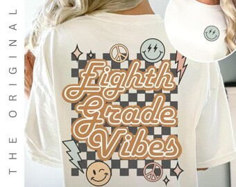 Puede incluir: Camiseta color crema con "Eighth Grade Vibes" en una fuente retro, sobre un fondo a cuadros. El diseño incluye caras sonrientes, símbolos de la paz y rayos. Un pequeño logotipo de carita sonriente está en el frente.