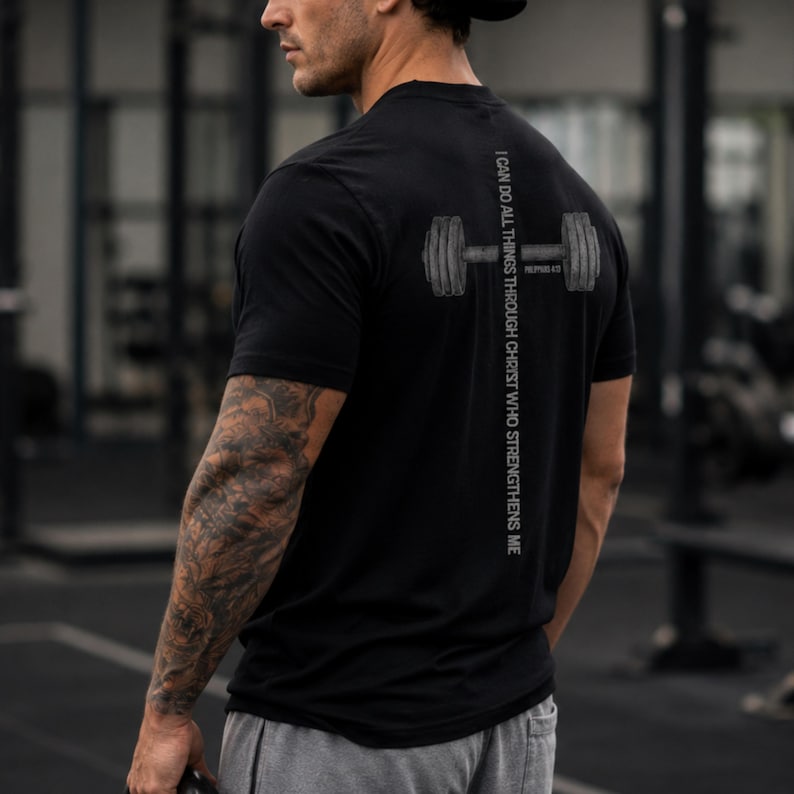 A man wearing a black t-shirt with a graphic design on the back, standing in a gym.