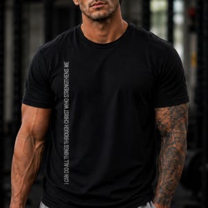 A man wearing a black t-shirt with text on it, standing in a gym setting.