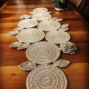 Peut inclure: Un chemin de table crocheté de couleur beige avec une série de motifs circulaires et de feuilles.