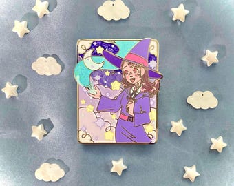 Puede incluir: Un pin de esmalte morado y rosa con una bruja de dibujos animados con un sombrero puntiagudo, sosteniendo una varita y lanzando un hechizo. El fondo es una escena caprichosa con estrellas, nubes y una luna creciente.