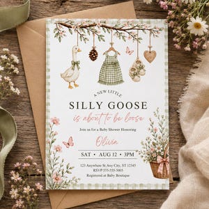 Könnte beinhalten: Eine Babyparty-Einladungskarte mit einer Aquarellillustration einer Gans, eines Kleides, Babyschuhen und einem Herz, die an einem Ast hängen. Der Text lautet A NEW LITTLE SILLY GOOSE is about to be loose, Join us for a Baby Shower Honoring Olivia, SAT AUG 12 3PM.